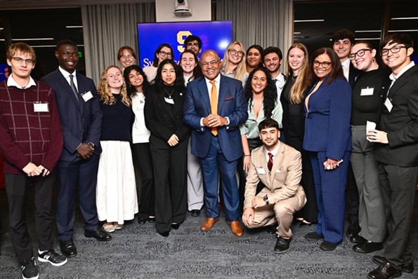 Newhouse and Maxwell students pose with Newhouse alumnus, Mike Tirico ‘88 at the grand opening of the Syracuse University Washington, DC center.  Tirico is currently the voice of NBC Sports’ biggest events, handling play-by-play for Sunday Night Football and serving as the primetime host for NBCUniversal’s coverage of the Olympics, the Kentucky Derby, and the U.S. Open amongst other major events. (https://www.nbcsports.com/pressbox/bios/mike-tirico)